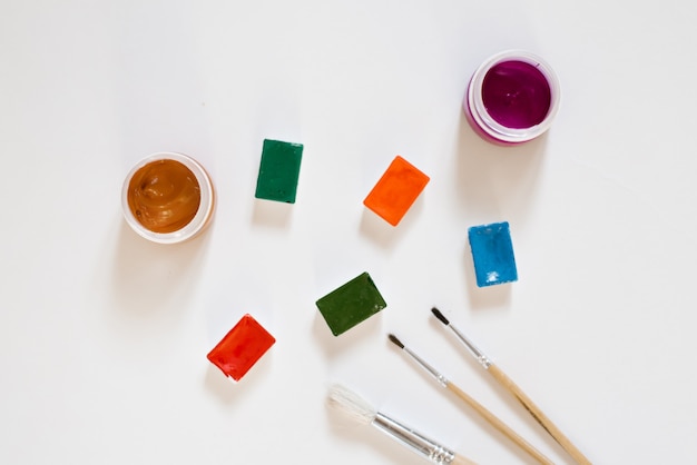 Акварельные краски разных цветов в рвах в белой коробке и кисти с деревянными ручками на белом фоне. Рисование и мастер-классы для художественной школы