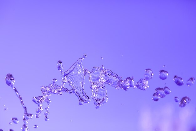 Waterdruppels bevroren in de lucht met spatten en kettingbubbels op een blauwe geïsoleerde achtergrond in de natuur Heldere en transparante vloeistof die gezondheid en natuur symboliseert