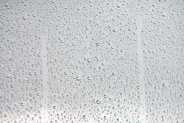 Waterdruppels op een vensterglas met een wolkenlucht op de achtergrond