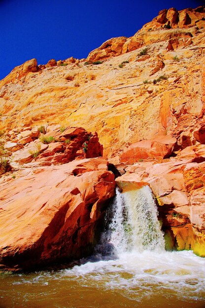 Waterfall by rocky mountain against clear sky