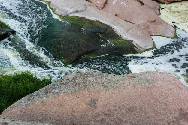 La cascata scorre tra alte rocce, pietre rosse e scogliere, cespugli e alberi verdi