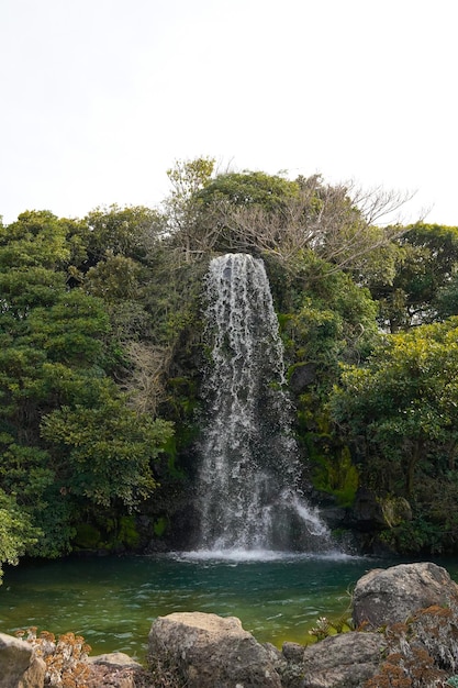 A waterfall in the forest with a man sitting on a bench in front of it.