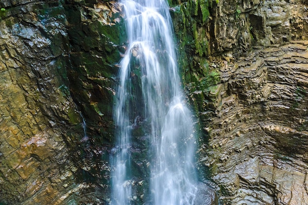 Waterfall on mountain river with white foamy water falling down from rocky formation in summer forest.