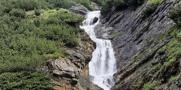 A waterfall in the mountains with green trees in the background