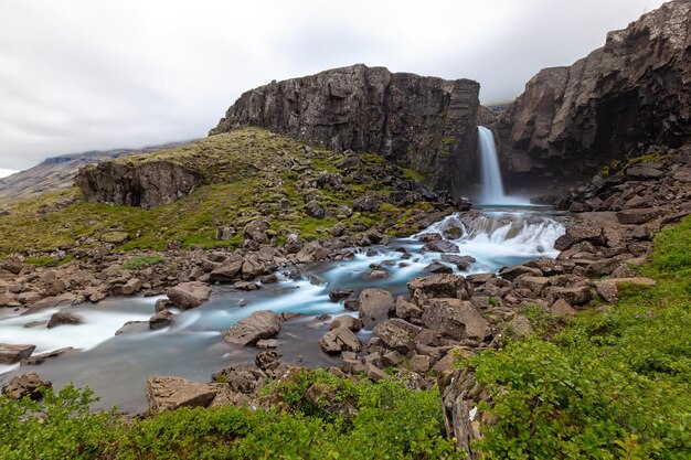 Cascata in un paese roccioso con cespugli verdi intorno in islanda