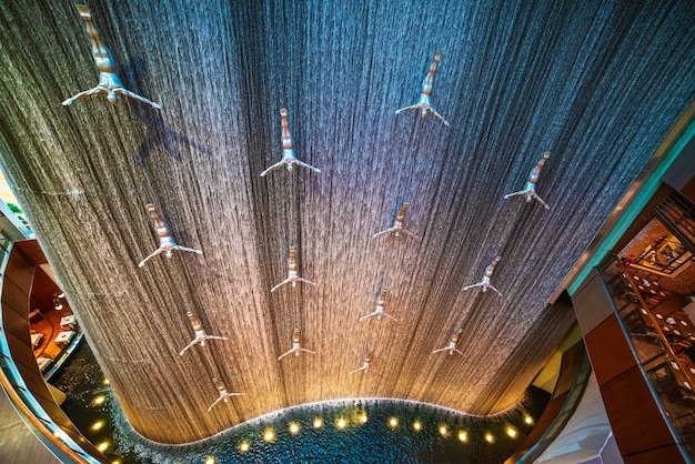 Photo waterfall with flying men in dubai mall in dubai, united arab emirates. travel attraction with colorful illumination