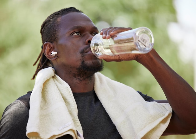 Waterfitness pauze en zwarte man die in de natuur rent, oefent hydratatie en focus op lichaamsprestaties in Duitsland Dorstige training en Afrikaanse hardloper denken aan cardiotraining in het park met een drankje