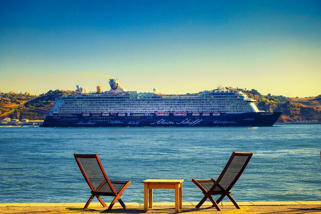 Photo waterfront view of a cruise ship with clear sky in front of relaxing chairs