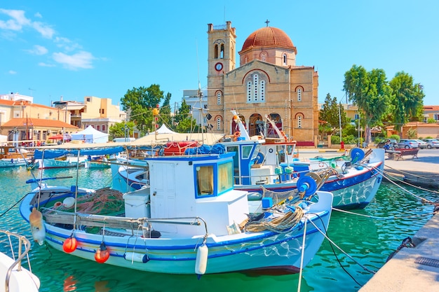 Waterfront with Ekklisia Isodia Theotokou Church in Aegina town and moored old fshing boats, Aegina Island, Greece