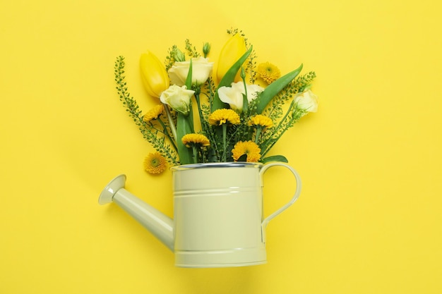 Watering can with flowers on yellow background