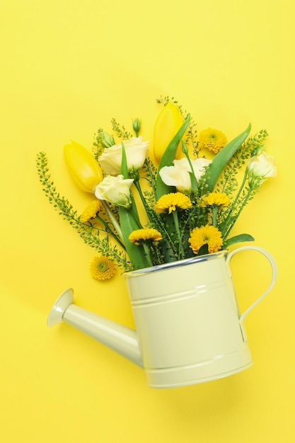 Watering can with flowers on yellow background