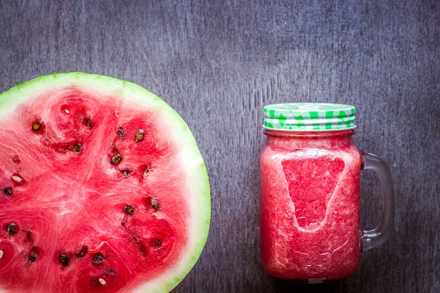 Watermeloen-smoothie en een halve verse watermeloen op een donkere houten ondergrond, plat of bovenaanzicht