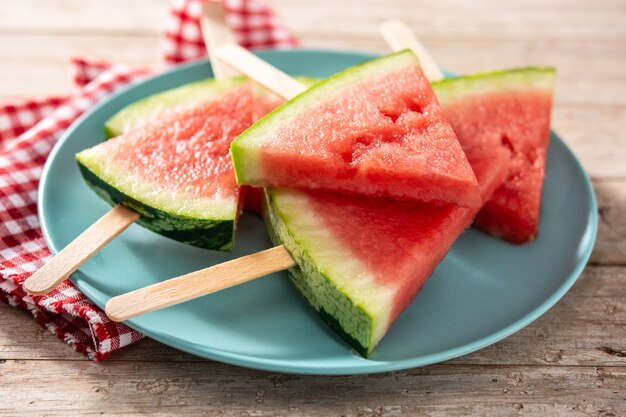 Watermeloen snijdt ijslolly's op blauwe plaat en houten tafel