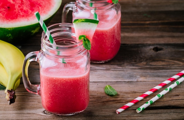 Watermelon and banana smoothie in mason jars with mint on wooden rustic background