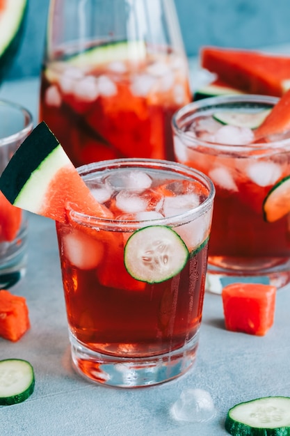 Watermelon cocktail in a glass with cucumber slice and ice cubes on the table. Refreshing drink