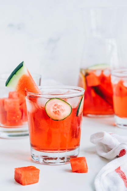 Watermelon cocktail in a glass with cucumber slice and ice cubes on the table. Refreshing drink