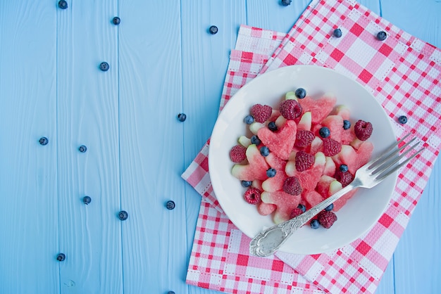 Watermelon in the form of hearts, raspberries, blueberries in a white plate.