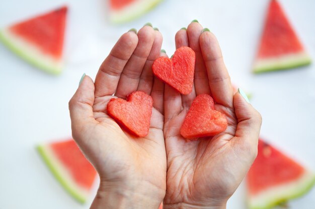 Fette di cuori di anguria sulle mani della donna fetta di anguria distesa su bianco amore e cura