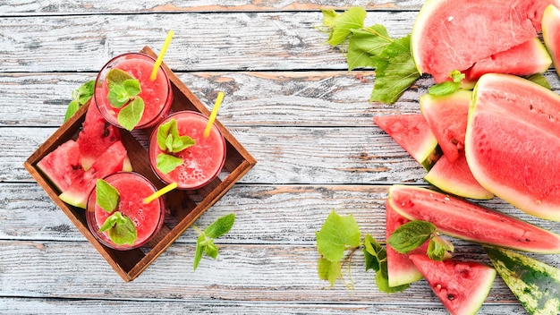 Succo di anguria con menta e ghiaccio in un bicchiere melone su fondo di legno bianco spazio libero per il testo vista dall'alto