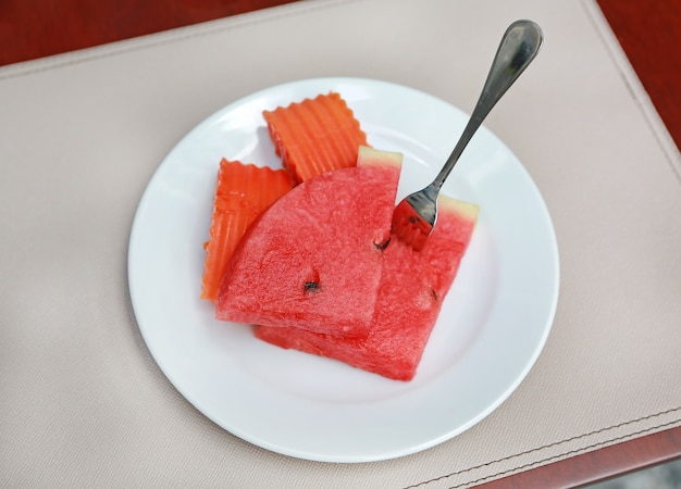Арбуз и кусочки папайи на тарелке с вилкой