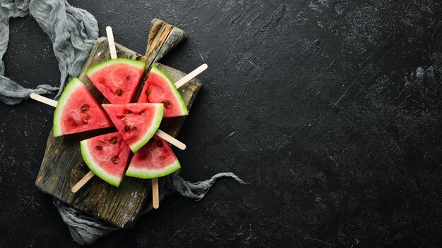 Watermelon popsicle on black background. Watermelon slices on sticks. Top view. Free copy space.