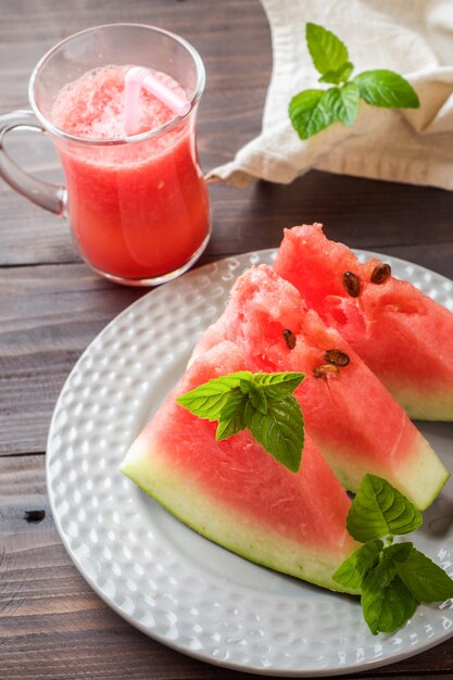 Watermelon sliced on a plate with mint leaves and fresh watermelon smoothie on a wooden background.