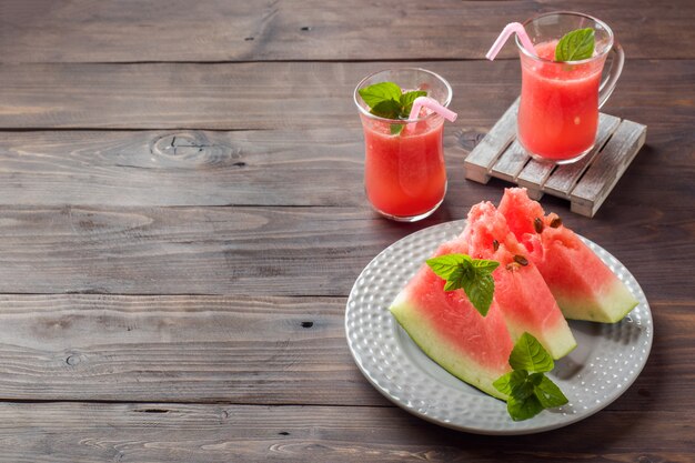 Watermelon sliced on a plate with mint leaves and fresh watermelon smoothie on a wooden background.