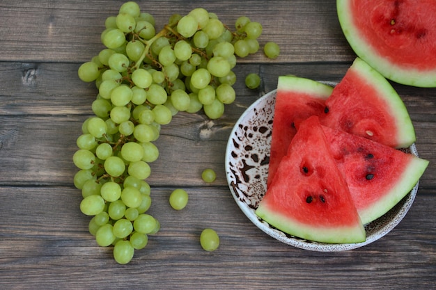 watermelon slices on plate and bunch of green grapes on dark wooden background