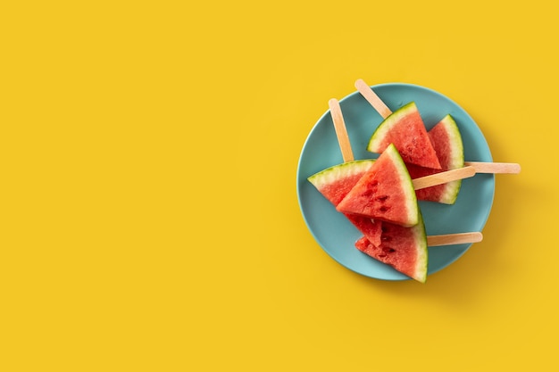 Watermelon slices popsicles on yellow surface