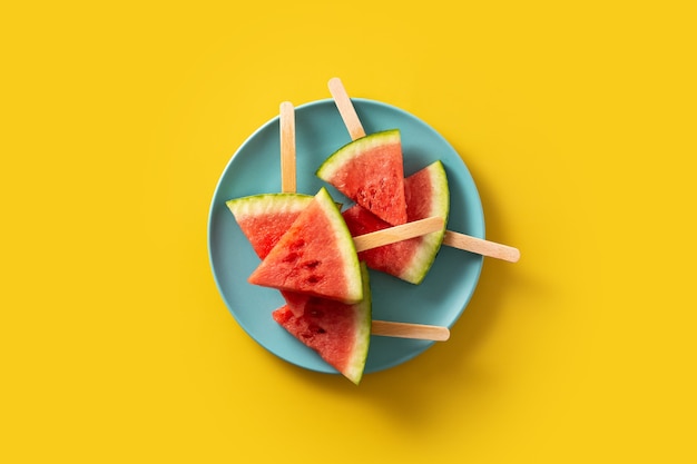 Watermelon slices popsicles on yellow surface