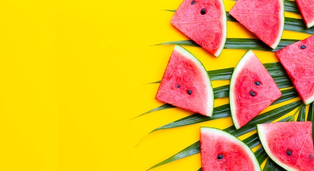 Watermelon slices on tropical palm leaves on yellow background. Summer background concept