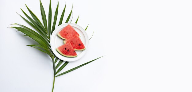 Watermelon slices on white plate with green leaves on white background.