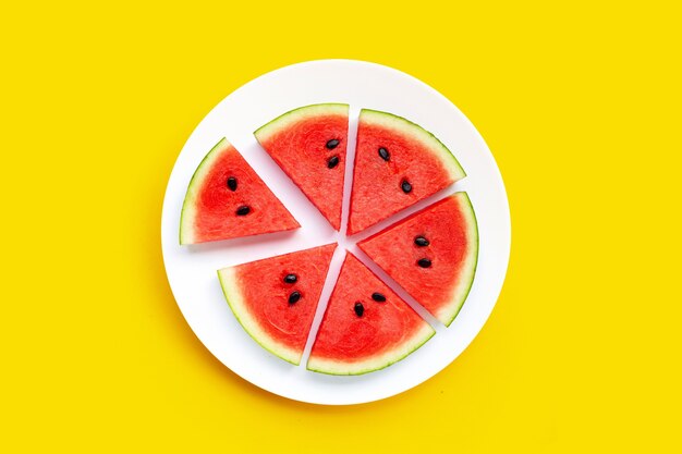 Watermelon slices in white plate on yellow background.