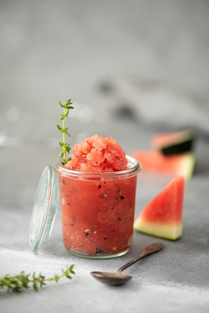 Watermelon smoothie with basil and thyme in glass jars on a grey table