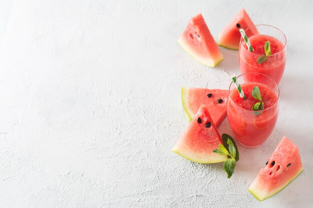 Watermelon smoothie with slice of fruit and leaf of mint over white