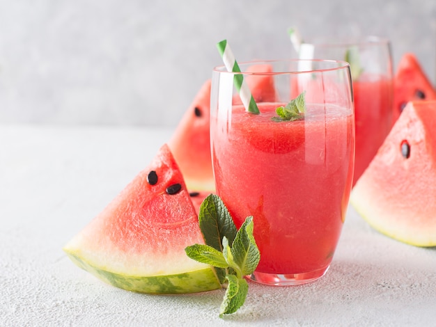 Watermelon smoothie with slice of fruit and leaf of mint over white