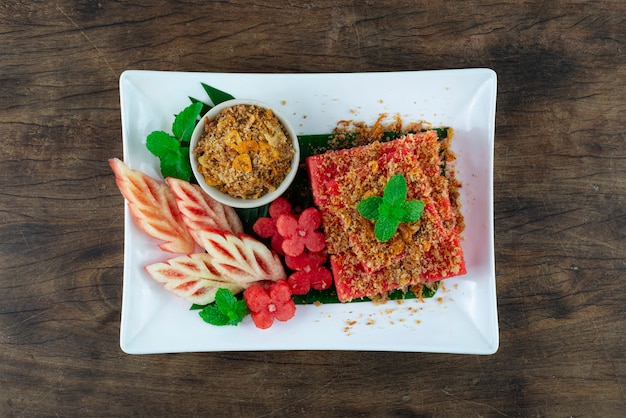 Арбуз со сладкой сушеной хрустящей рыбой и чесночным соусом в белой тарелке на деревянном фоне, вид сверху