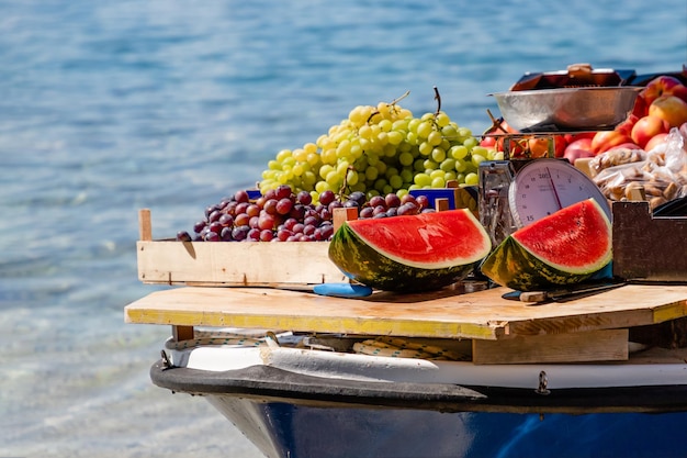 Foto watermelons groene en paarse druiven perziken in een boot op een heldere zee achtergrond