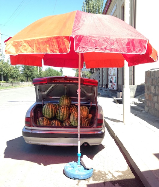 Photo watermelons for sale in car in front of red umbrella on sunny day