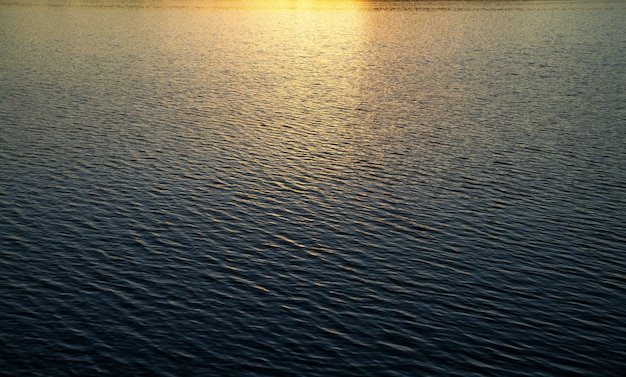 Wateroppervlak met golven onder de stralen van de ondergaande zon.