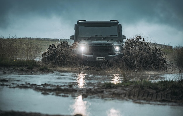 Waterplons in offroad racen klassieke x auto die water oversteekt met spatten op modderige weg lage hoek vi