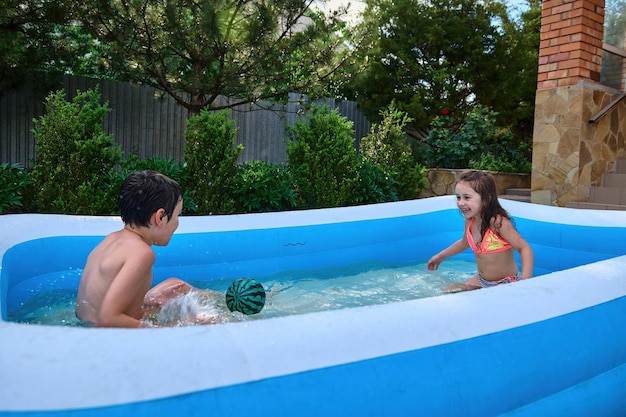 Waterpretdag in een achtertuin Gelukkige kinderen die een bal spelen en elkaar met water bespatten in een opblaasbaar zwembad