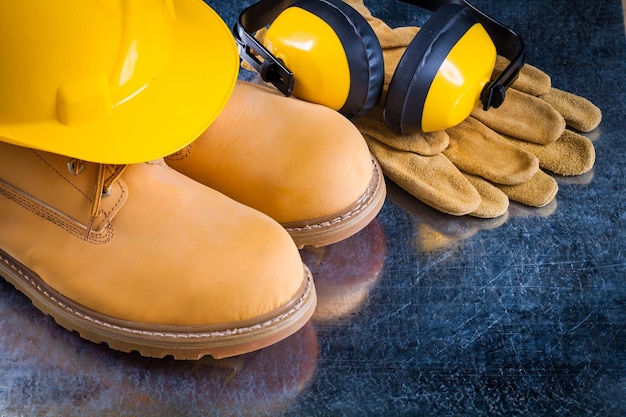 Waterproof boots leather protective gloves earmuffs and building helmet on scratched metallic background construction concept