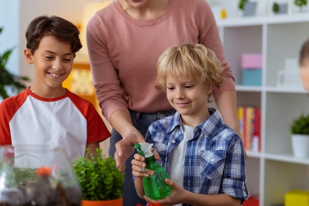 Waterverspreider vasthouden. schattige blonde leerling die waterverspreider vasthoudt terwijl ze de plant water geeft tijdens de ecologieles