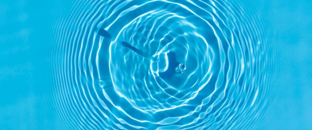 Wave from a drop of water on blue water under natural light. Top view, flat lay.