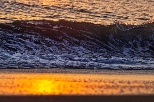 A wave is breaking on the beach and the sun is setting.