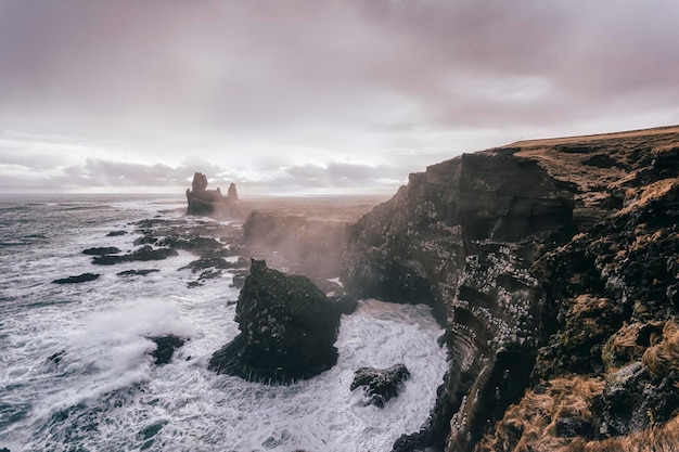 Wave splashing on cliff against cloudy sky