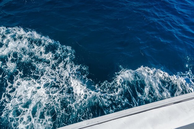Photo wave trace with white foam on a water surface behind of fast moving yacht