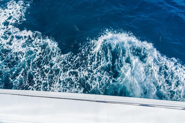 Wave trace with white foam on a water surface behind of fast moving yacht