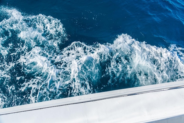 Wave trace with white foam on a water surface behind of fast moving yacht